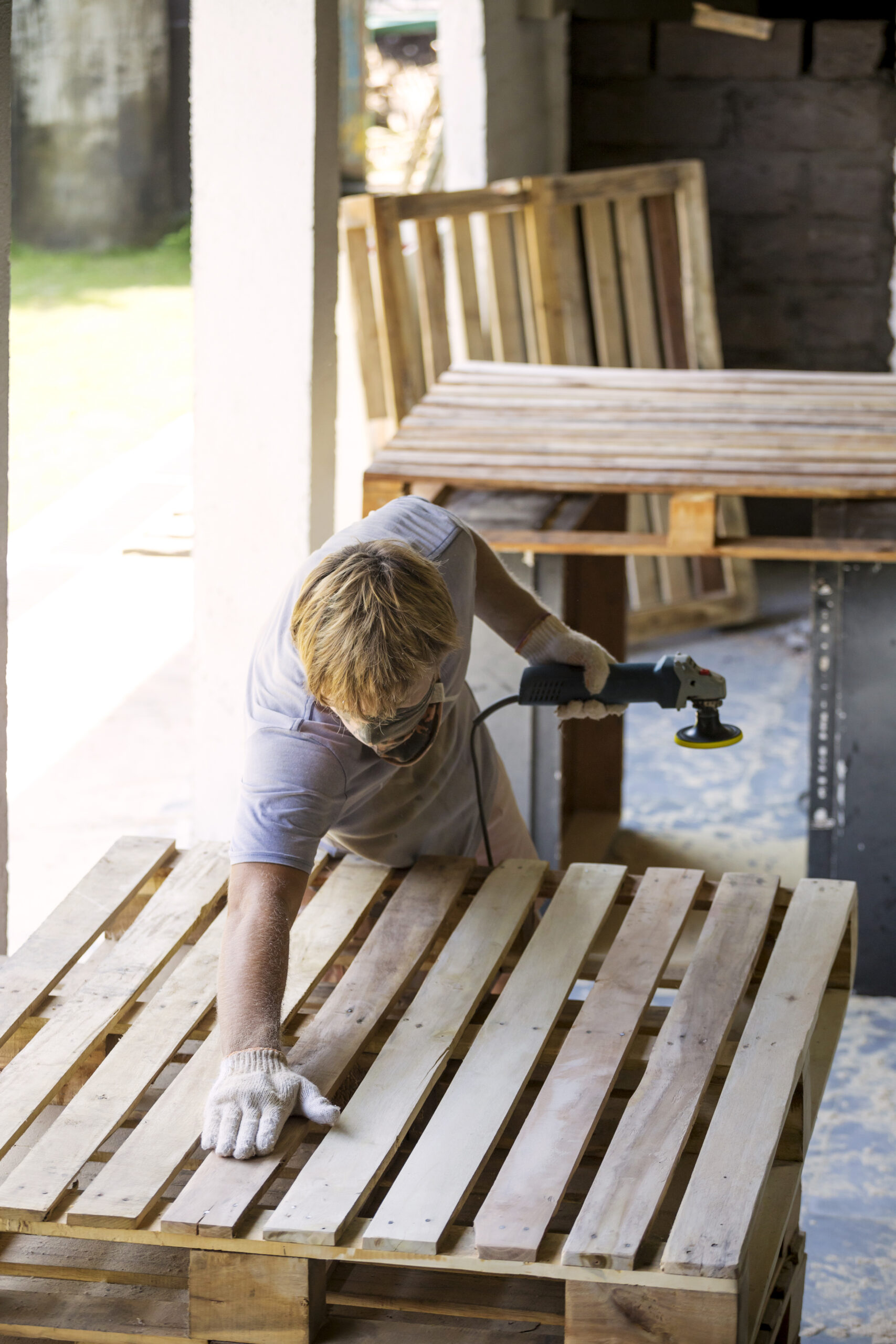 Hombre lijando un palé con una lijadora orbital aleatoria.
