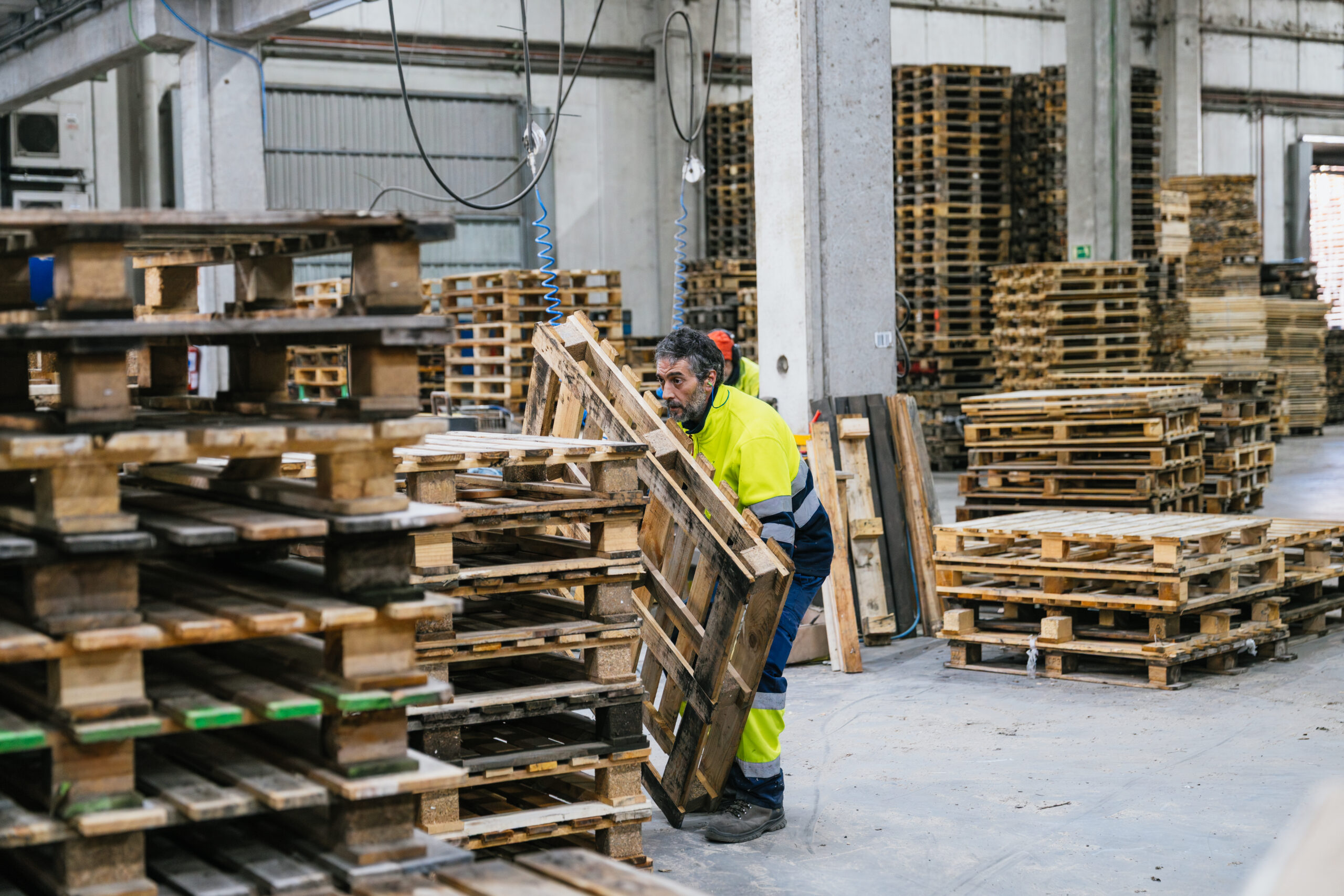 Trabajador manipulando palés de madera en fábrica de reciclaje.